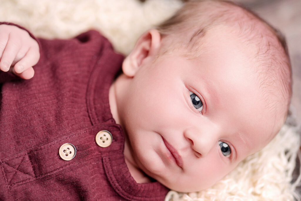 Newborn baby boy curled up in womb pose on textured blanket in professional studio setting
