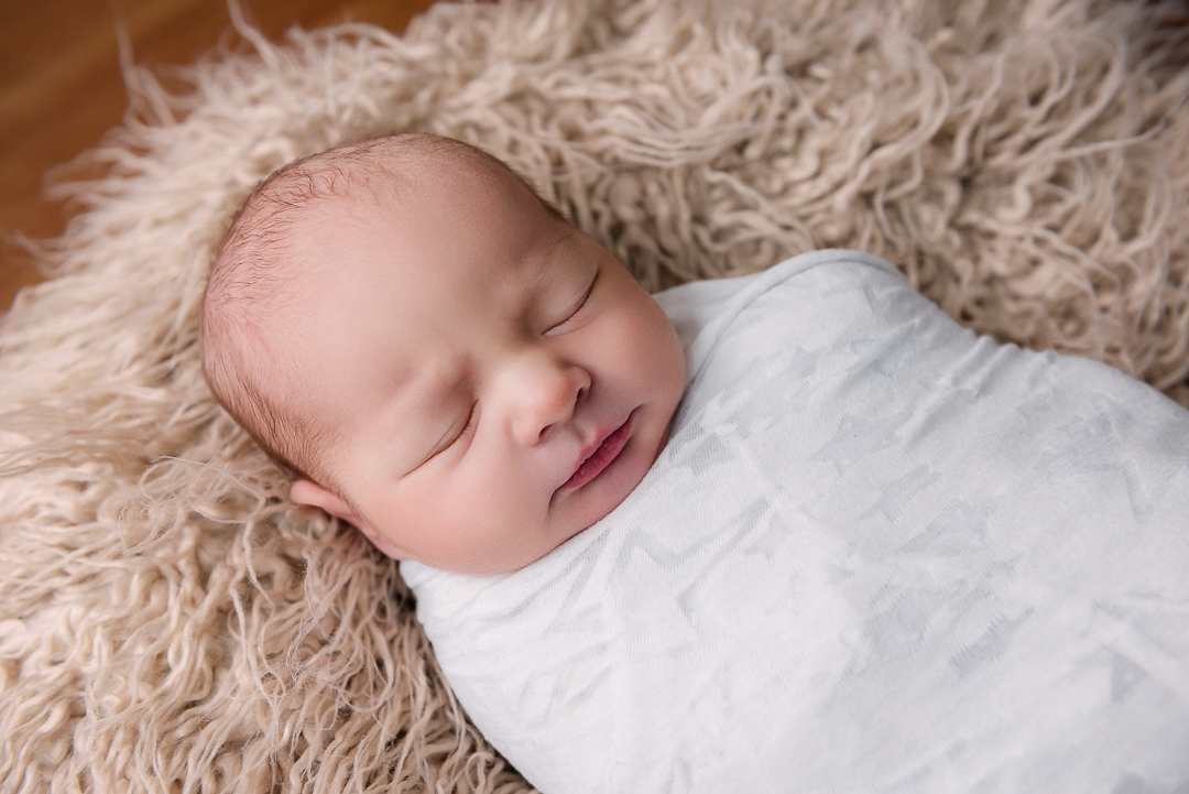 Newborn photographer gently wrapping baby using safe techniques in Hudson WI